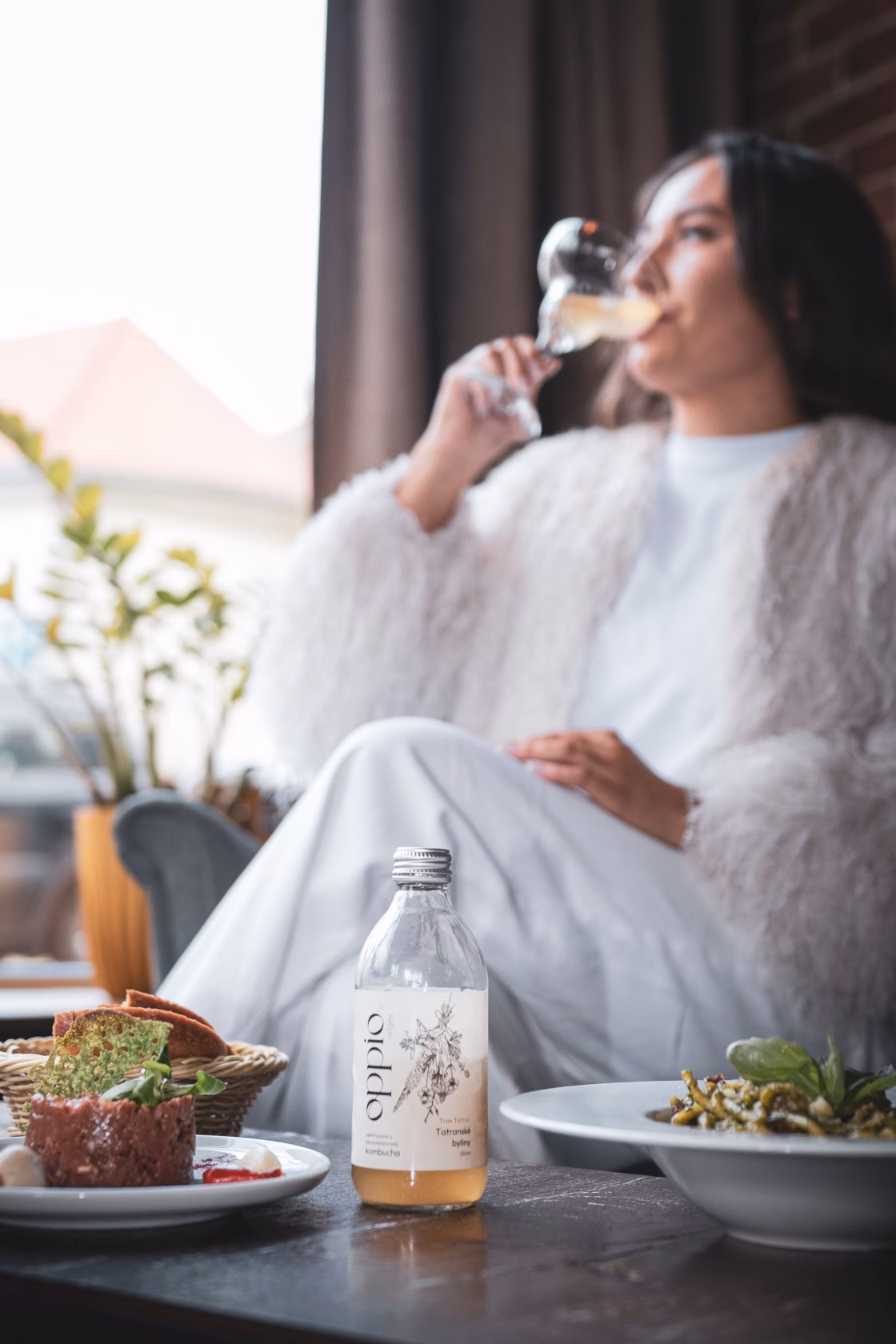 Hostka pije kombuchu oppio. z poháru při obědě v restauraci